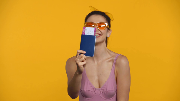 Happy girl in swimsuit pointing on passport and air ticket isolated on yellow - Footage, Video