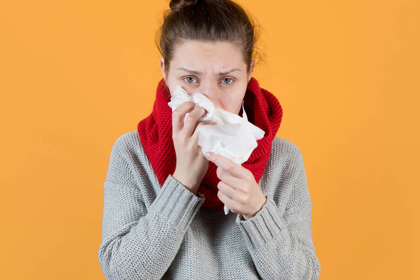 sick girl looks sadly at the camera and holds a scarf near her nose on yellow background - Foto, Bild
