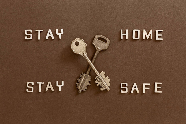 Words Stay home Stay safe made from wooden letters and two keys, concept of self quarantine at home as preventative measure against  corona virus Covid 19 outbreak. Staying at home  during pandemic - 写真・画像