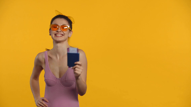усміхнена дівчина в купальнику вказує на паспорт і авіаквиток ізольовано на жовтому
 - Кадри, відео