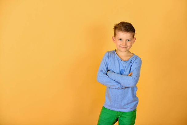 Λαμπερό και κομψό αγόρι που ποζάρει για την κάμερα, μοντέλο με μπλε ρούχα στο στούντιο σε κίτρινο φόντο. - Φωτογραφία, εικόνα