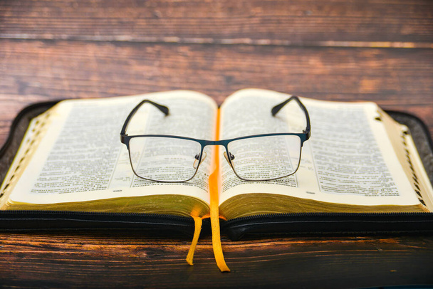 Η Αγία Γραφή και τα γυαλιά, γυαλιά για την όραση βρίσκονται στην ανοιγμένη Αγία Γραφή ενός θέματος δώρου με επίχρυσες σελίδες. - Φωτογραφία, εικόνα