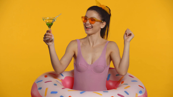 Uśmiechnięta dziewczyna w stroju kąpielowym tańczy i trzyma koktajl odizolowany na żółto - Materiał filmowy, wideo