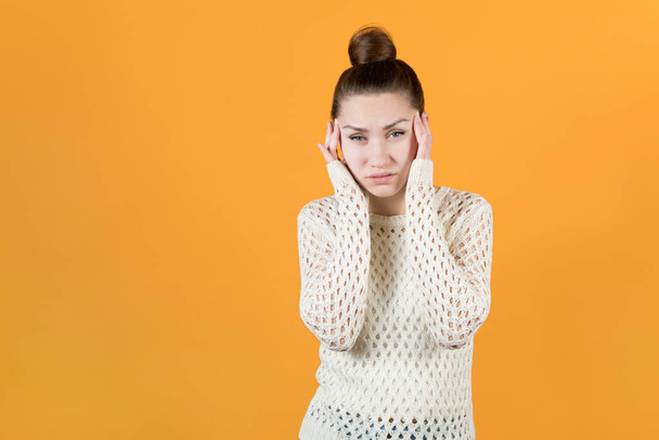 A young girl in a white sweater is holding her head on a yellow background. isolated on yellow background - 写真・画像