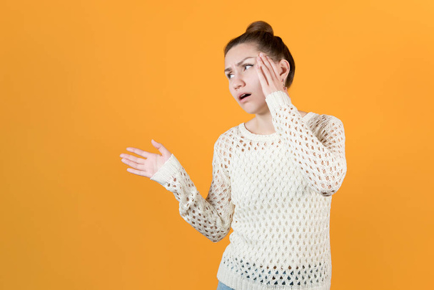 the girl holds on to her head and looks away with hope. Girl with a sore head is waiting for help, holding out her hand. Isolated on yellow background - Photo, Image