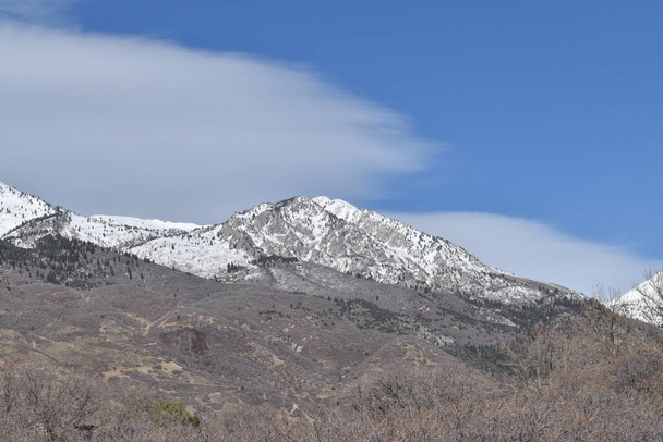 麓は茶色い雪の山と白い雲が浮かぶ青い空.  - 写真・画像