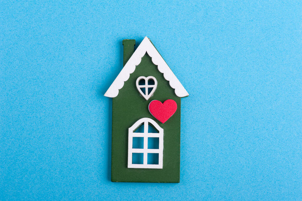 Green wooden house and heart on blue background with copy space. Safety or quarantine concept, home protection, real estate insurance, private property - Photo, Image