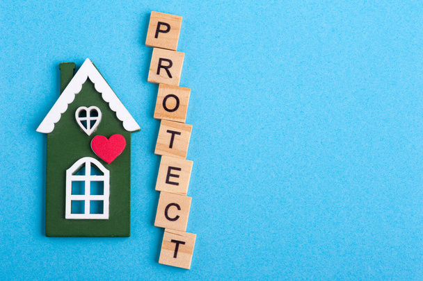 Green wooden house and Protect sign on blue background with copy space. Safety or quarantine concept, home protection, real estate insurance, private property - Photo, Image