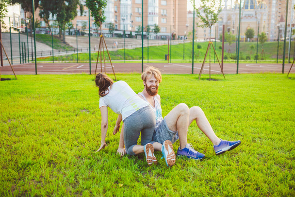 夏の公園で芝生の上で訓練した後、若い白人のカップルが遊び、喜びます。合同訓練のテーマ。健康的な運動家族。若いスポーツカップル一緒に屋外で幸せ. - 写真・画像