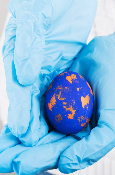 Tiempo de Pascua en concepto de cuarentena. Mano femenina en guantes médicos azules sosteniendo huevos de Pascua. Concepto de vacaciones de Pascua y vacaciones de primavera durante el coronavirus
 - Foto, imagen