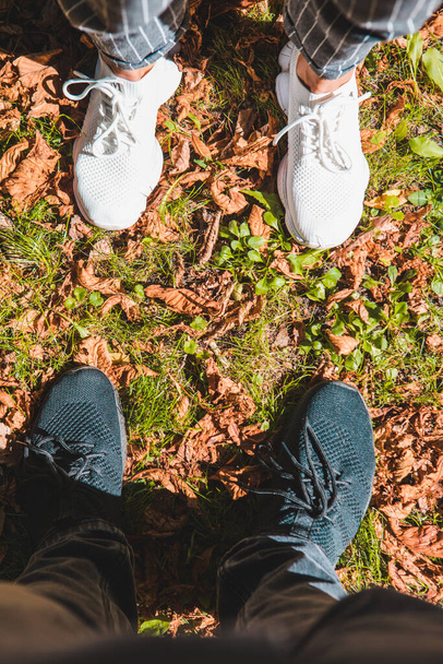 gambe uomo e donna in sneakers bianche e nere su erba verde con foglie rosse arrugginite. copia spazio
 - Foto, immagini