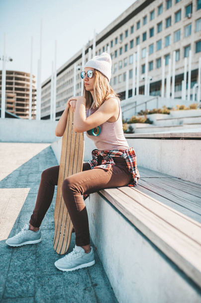 Attractive woman in a hat relaxing on the steps after longboard riding. - Foto, Imagem