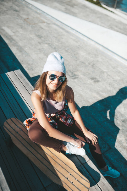 Atrakcyjna kobieta w kapeluszu relaksująca się na schodach po longboardzie. - Zdjęcie, obraz