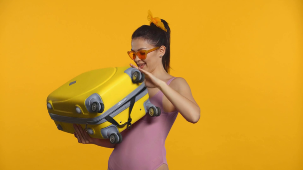 Zaskoczona dziewczyna w stroju kąpielowym otwiera walizkę izolowaną na żółto - Materiał filmowy, wideo