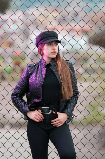 American portrait of young woman and long hair dressed in black clothes and leather jacket resting on racks - Foto, Imagem