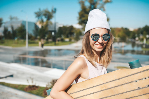 Porträt einer attraktiven Frau mit Hut und Sonnenbrille mit Longboard im Freien - Foto, Bild