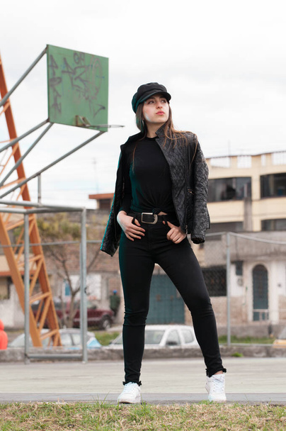 バスケットボールコートの後ろに服と黒の帽子を持つ女性の都市の肖像画 - 写真・画像