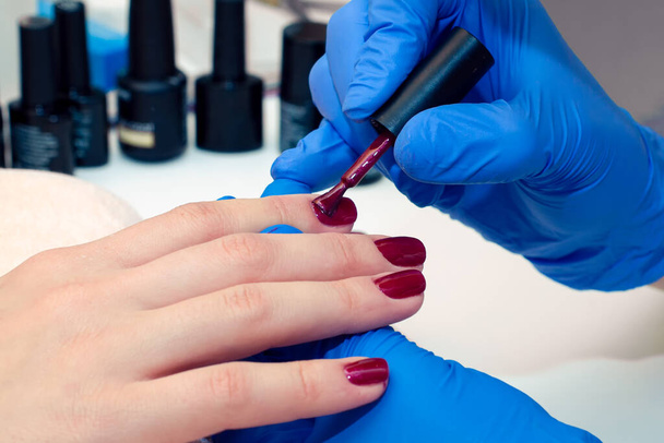 manicure specialist covers the nails with red varnish. close up - Fotografie, Obrázek