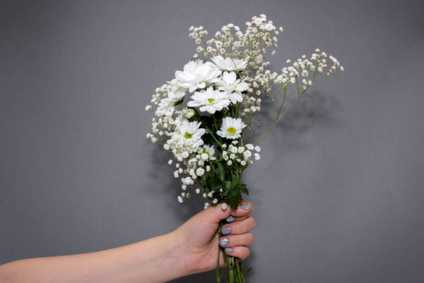 Woman holding bouquet with gypsophila and daisy on gray background - Zdjęcie, obraz