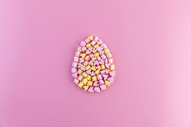 Single multicolored easter egg made of small marshmallows hearts on a pink background. Concept. - Zdjęcie, obraz