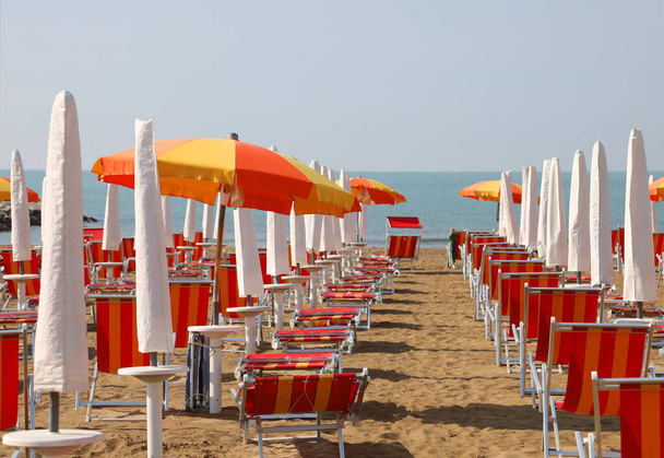 İnsanlar olmadan bir turist köyünün özel plajında sıra sıra sandalye ve şemsiyeler. - Fotoğraf, Görsel