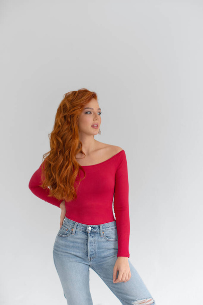 Young red-haired girl in jeans and a red bodysuit posing in a bright roo - Zdjęcie, obraz