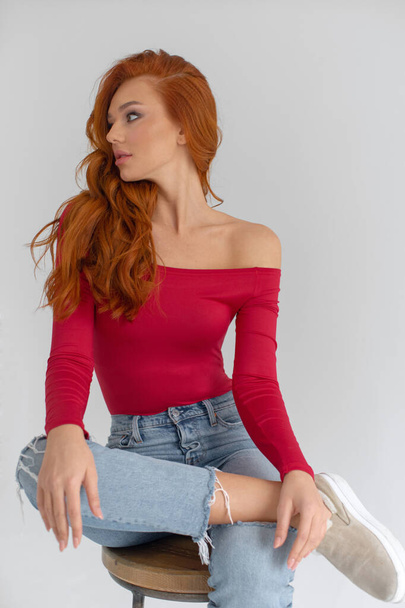Young red-haired girl in jeans and a red bodysuit posing in a bright roo - Foto, immagini
