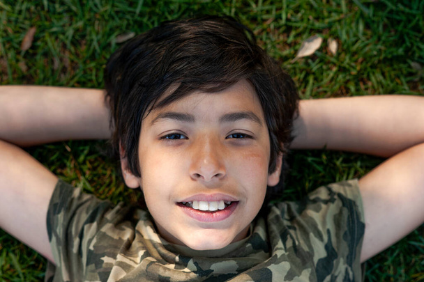 χαριτωμένο νεαρό αγόρι κοντά ξαπλωμένο στο γρασίδι σε μια ηλιόλουστη μέρα. - Φωτογραφία, εικόνα