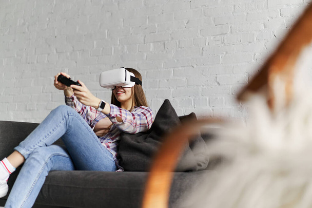 Молодая улыбающаяся женщина в очках VR играет в игру с помощью джойстика, дополненной реальности
 - Фото, изображение