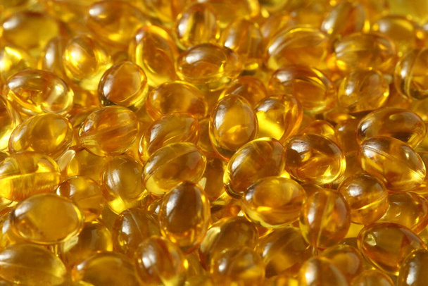 Gouden achtergrond capsules Close-up voedingssupplement olie gevulde capsules geschikt vitamine A, vitamine D3, visolie, omega 3, 6, 9, teunisbloem, bernagie olie, lijnzaadolie, vitamine D, vitamine E. - Foto, afbeelding