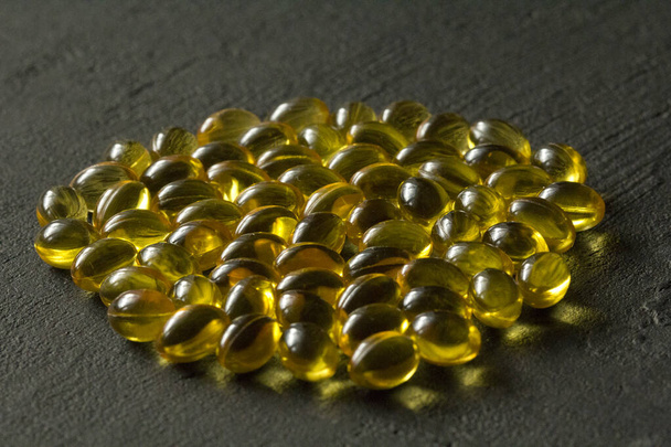 Pile of transparent capsules of golden yellow color lies on black modern background. Oil filled capsules vitamin A, vitamin D3, fish oil, omega 3, 6, 9, evening primrose, vitamin D, vitamin E. - Photo, Image