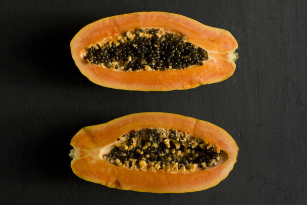 Zwei Hälften der Papaya-Frucht, halbiert, liegen auf schwarzem, modernem Hintergrund. Schwarze Samen süßer, orangefarbener Papaya. Vegetarismus, gesunde Ernährung, Ernährung. Tropische Früchte. Draufsicht. Kopierraum. Flache Lage. - Foto, Bild