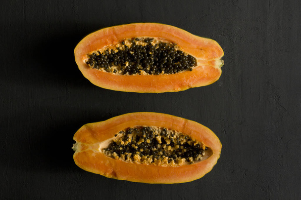パパイヤの果実の半分にカットの2つの半分は、黒の現代的な背景に横たわっている。甘い、オレンジのパパイヤの黒い種。菜食主義、健康的な栄養、食事。熱帯果実。トップビュー。コピースペース。平敷. - 写真・画像