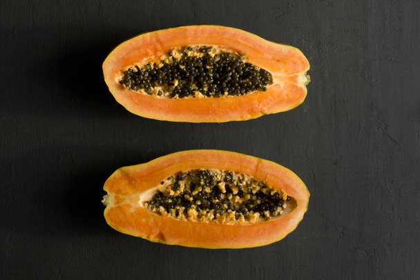 Two halves of papaya fruit cut in half, lie on black modern background. Black seeds of sweet, orange papaya. Vegetarianism, healthy nutrition, diet. Tropical fruits.Top view. Copy space. Flat lay. - Photo, Image