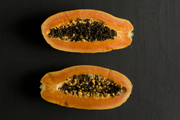 Two halves of papaya fruit cut in half, lie on black modern background. Black seeds of sweet, orange papaya. Vegetarianism, healthy nutrition, diet. Tropical fruits.Top view. Copy space. Flat lay. - Photo, Image