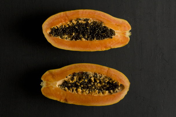 Két fél papaya gyümölcs félbevágva, fekszenek a fekete modern háttérben. Édes, narancsos papaya fekete magjai. Vegarianizmus, egészséges táplálkozás, diéta. Trópusi gyümölcsök.Top nézet. Másold a helyet. Lapos fektetés. - Fotó, kép
