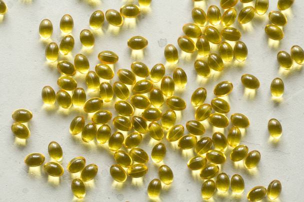 Montón de cápsulas transparentes de color amarillo dorado se encuentra en el fondo moderno gris claro. Cápsulas llenas de aceite vitamina A, vitamina D3, aceite de pescado, omega 3, 6, 9, onagra, vitamina D, vitamina E
. - Foto, imagen