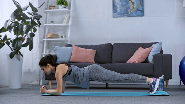 Side view of sportswoman doing plank on fitness mat in living room - Materiał filmowy, wideo
