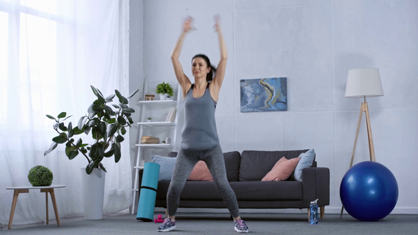 Usmívající se sportovkyně skákání při tréninku v obývacím pokoji - Záběry, video