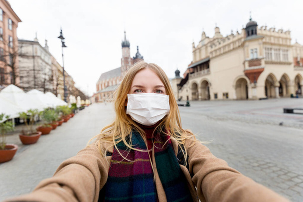 Stylowa blondynka w masce robiąca selfie przed słynną Bazyliką św. Marii na Rynku w Krakowie. Koncepcja epidemii koronawirusa. Kwarantanna w mieście - Zdjęcie, obraz
