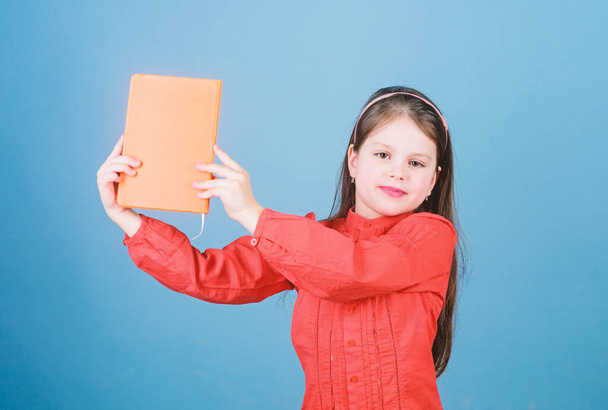 Look at this book. Small pupil took the book from library. Adorable school child with activity book. Cute little girl holding note book with orange cover, copy space - Fotoğraf, Görsel