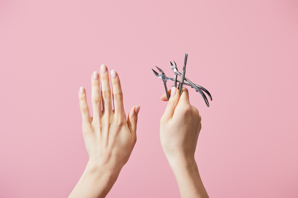 Cropped view of woman holding cuticle pusher and nippers isolated on pink - Photo, Image