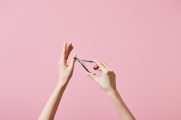 Partial view of woman cutting cuticle with nipper isolated on pink - Fotografie, Obrázek