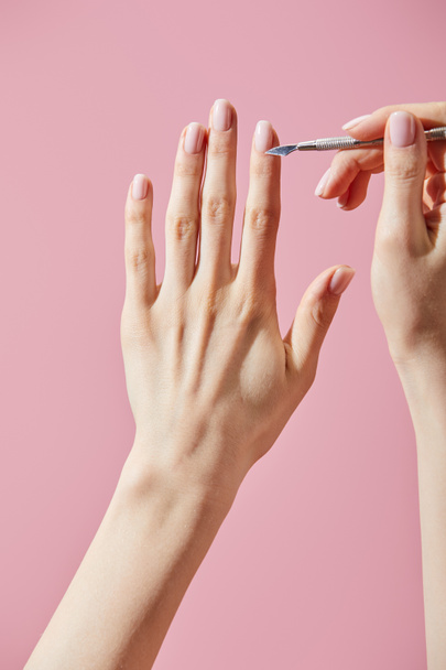 Vista parcial de la mujer haciendo manicura con empujador de cutícula aislado en rosa
 - Foto, Imagen