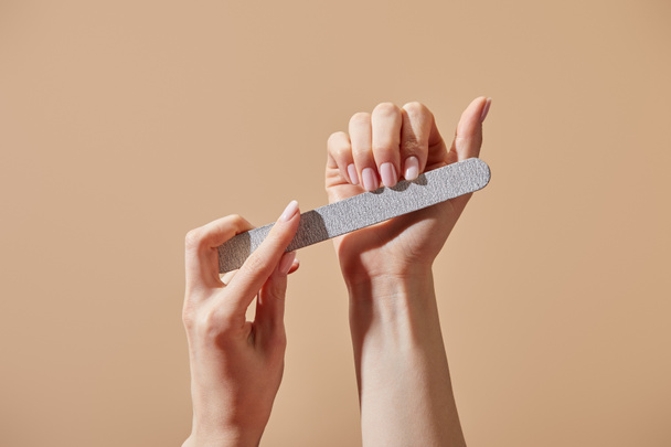 Partial view of woman filing fingernails with emery board isolated on beige - Photo, Image