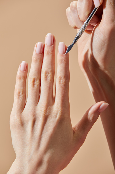 Cropped view of woman doing manicure with cuticle pusher isolated on beige - Zdjęcie, obraz