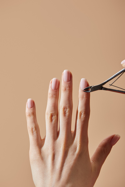 Partial view of woman doing manicure using cuticle nipper isolated on beige - Fotografie, Obrázek
