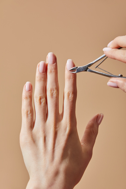 Partial view of woman using cuticle nipper isolated on beige - Valokuva, kuva
