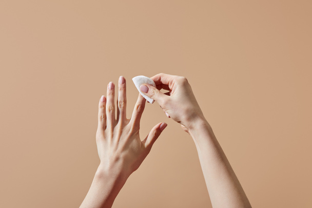 Vista parcial de la mujer quitando esmalte de uñas con almohadilla de algodón aislado en beige
 - Foto, imagen