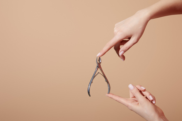 Cropped view of woman holding cuticle nipper isolated on beige - Foto, Bild